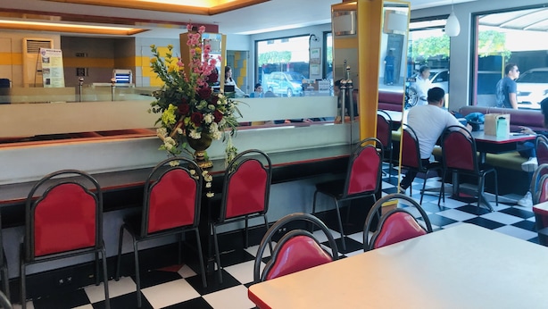 A restaurant with a checkered floor, red chairs, a central flower arrangement, and a counter with a mirror. - Park Bed and Breakfast Hotel Pasay (Pasay)