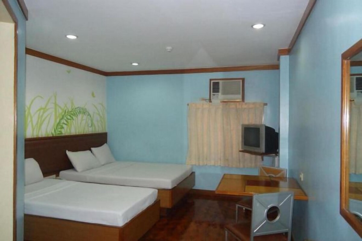Habitación de hotel con dos camas individuales, una mesa de madera, un televisor y un aire acondicionado instalado en la pared.