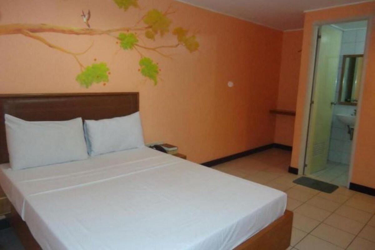 Habitación de hotel con cama, mesita de noche, teléfono fijo en la pared y puerta que da a un baño.
