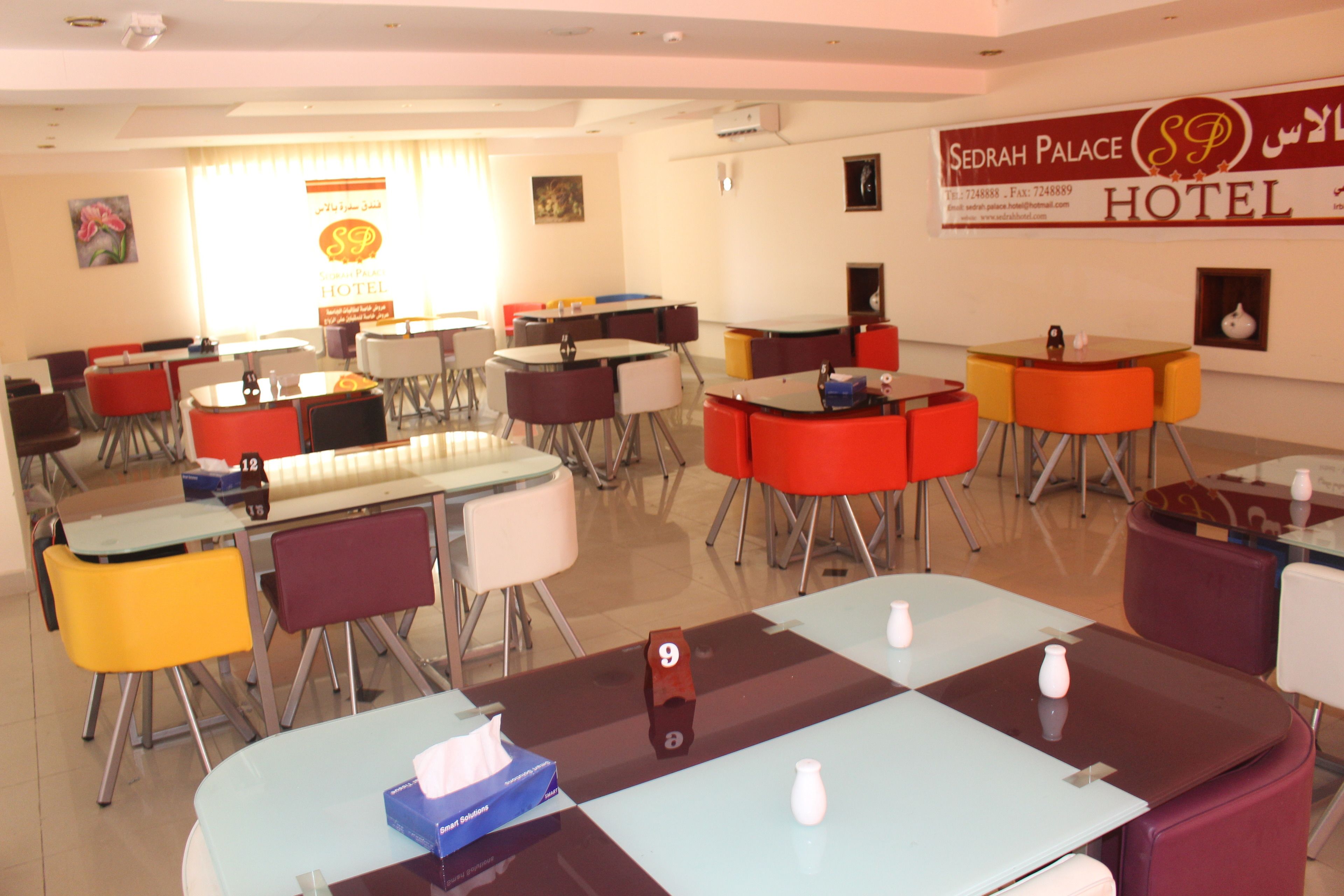 Une salle à manger d’hôtel avec plusieurs tables et chaises, un numéro de chambre bien visible et une enseigne indiquant « Sedrah Palace Hotel ».