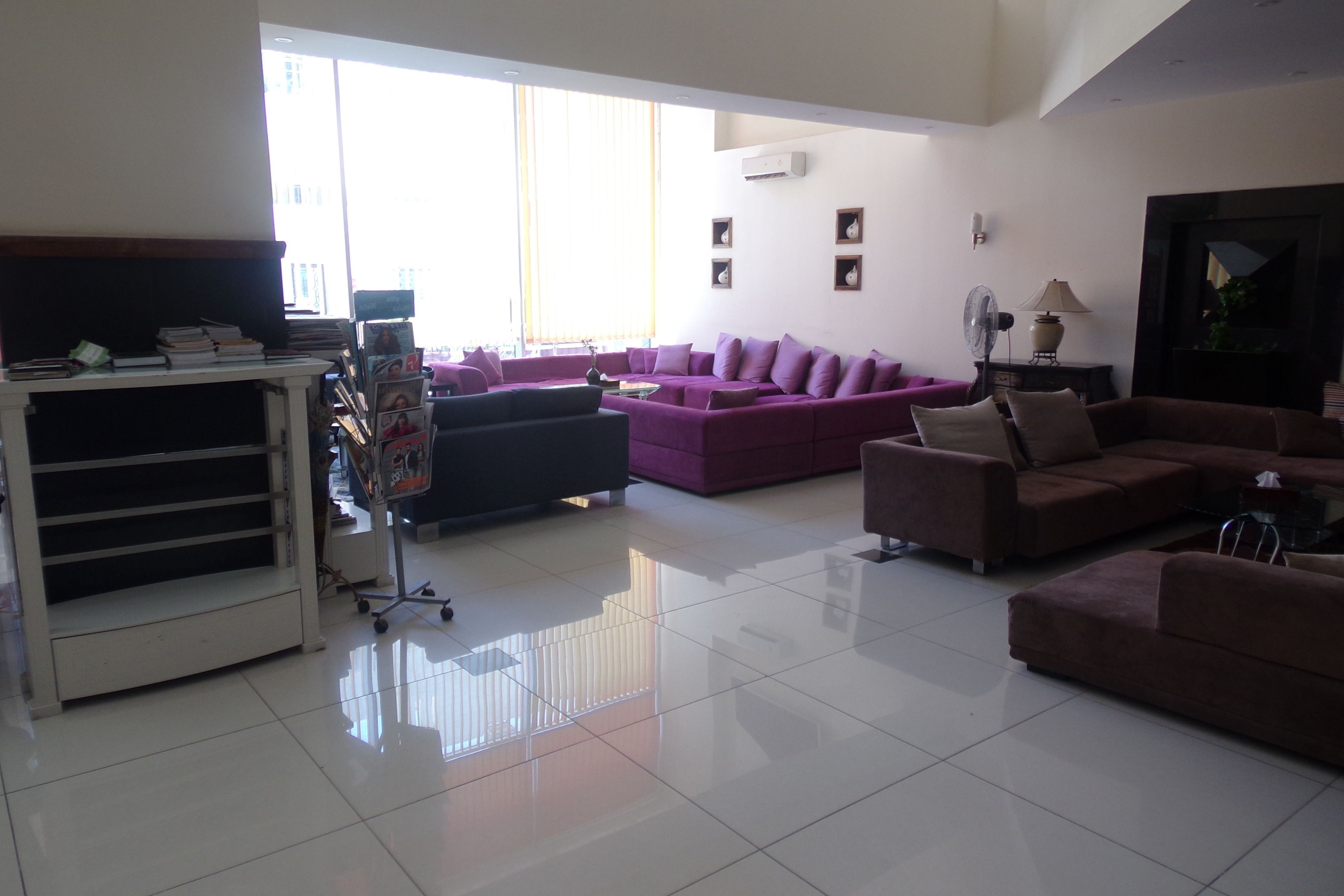 A spacious living room with a large window, a white tiled floor, and multiple couches.