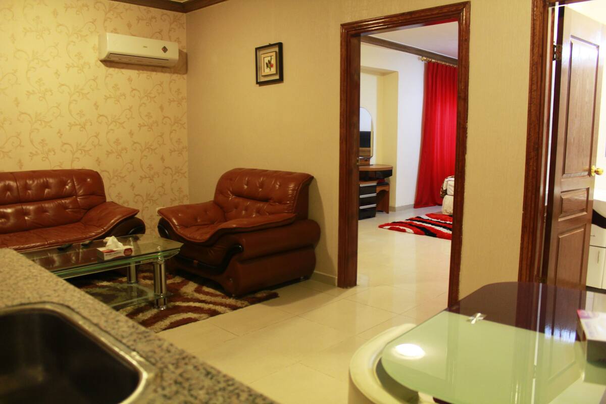 A living room with two leather sofas, a glass coffee table, and a wooden door leading to another room.