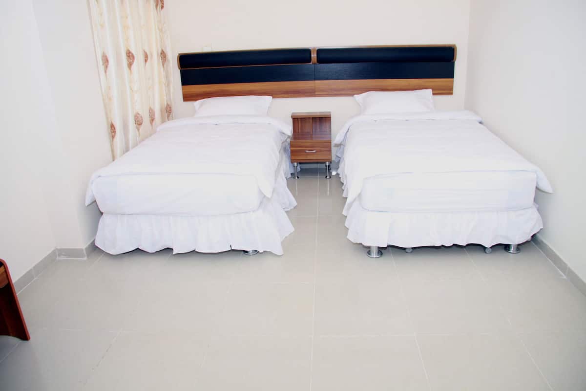A hotel room with two single beds, a wooden headboard, a small bedside table, and a curtain.