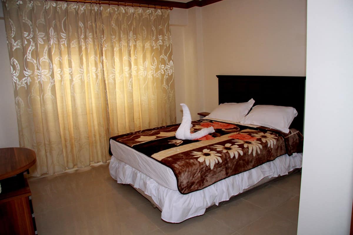 A neatly made bed with a floral bedspread and a swan-shaped pillow.