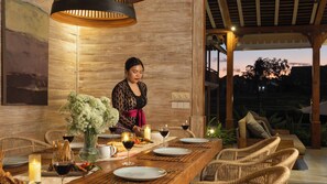 A dining area with a table set for two, featuring a vase of flowers, candles, and wine glasses.
