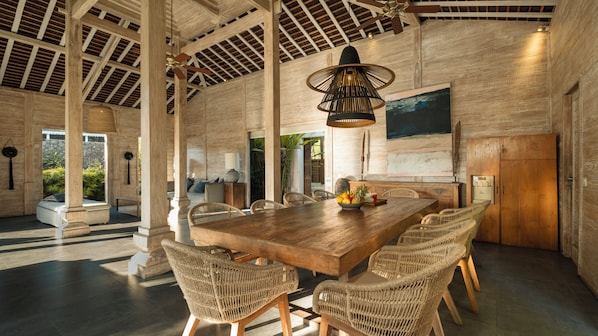 A spacious dining area with a large wooden table, wicker chairs, and a modern pendant light.