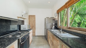 Cocina compacta con estufa a gas, microondas, refrigerador y ventana con vista a áreas verdes.
