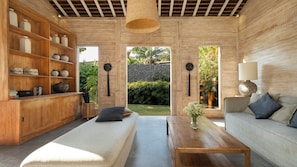 Una sala de estar moderna con un sofá, una mesa de centro y una estantería. Se ve un jardín a través de un ventanal.