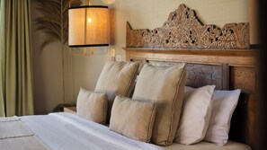 A hotel room with a bed, pillows, a headboard with intricate carvings, a wall-mounted lamp, and a nightstand. - Villa Alea by Villa Finder (Kerobokan)