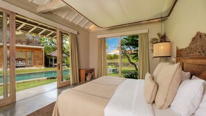 Un dormitorio con una cama grande, vista a una piscina y estructura de techo de madera.
