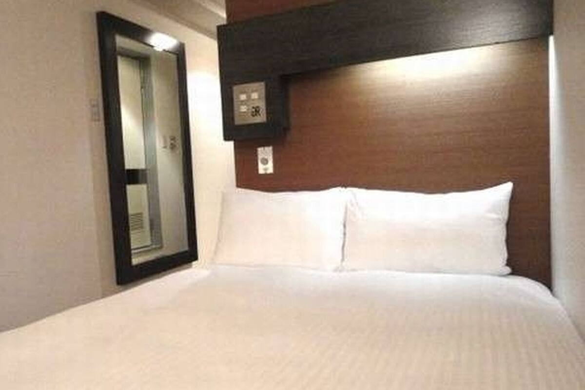 A hotel room with a bed, a mirror, and a wooden headboard.