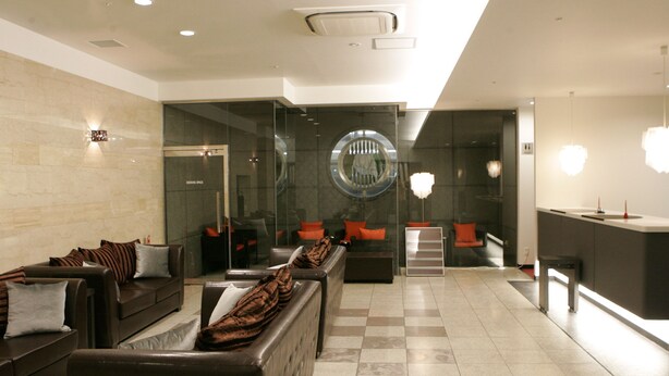 A modern hotel lobby with a checkered floor, leather sofas, a reception desk, and a large mirror.