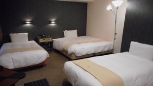 A hotel room with three beds, a desk, and a lamp.