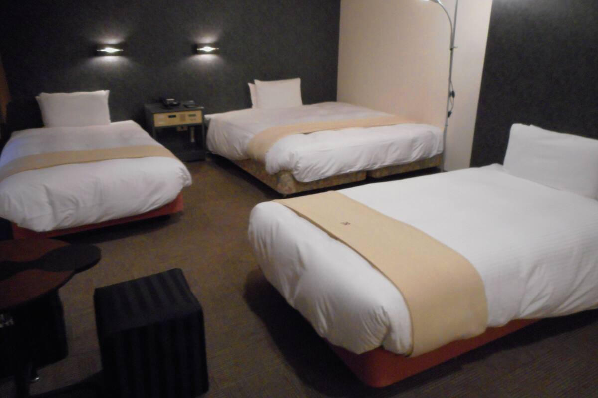 A hotel room with three beds, a desk, and a lamp.