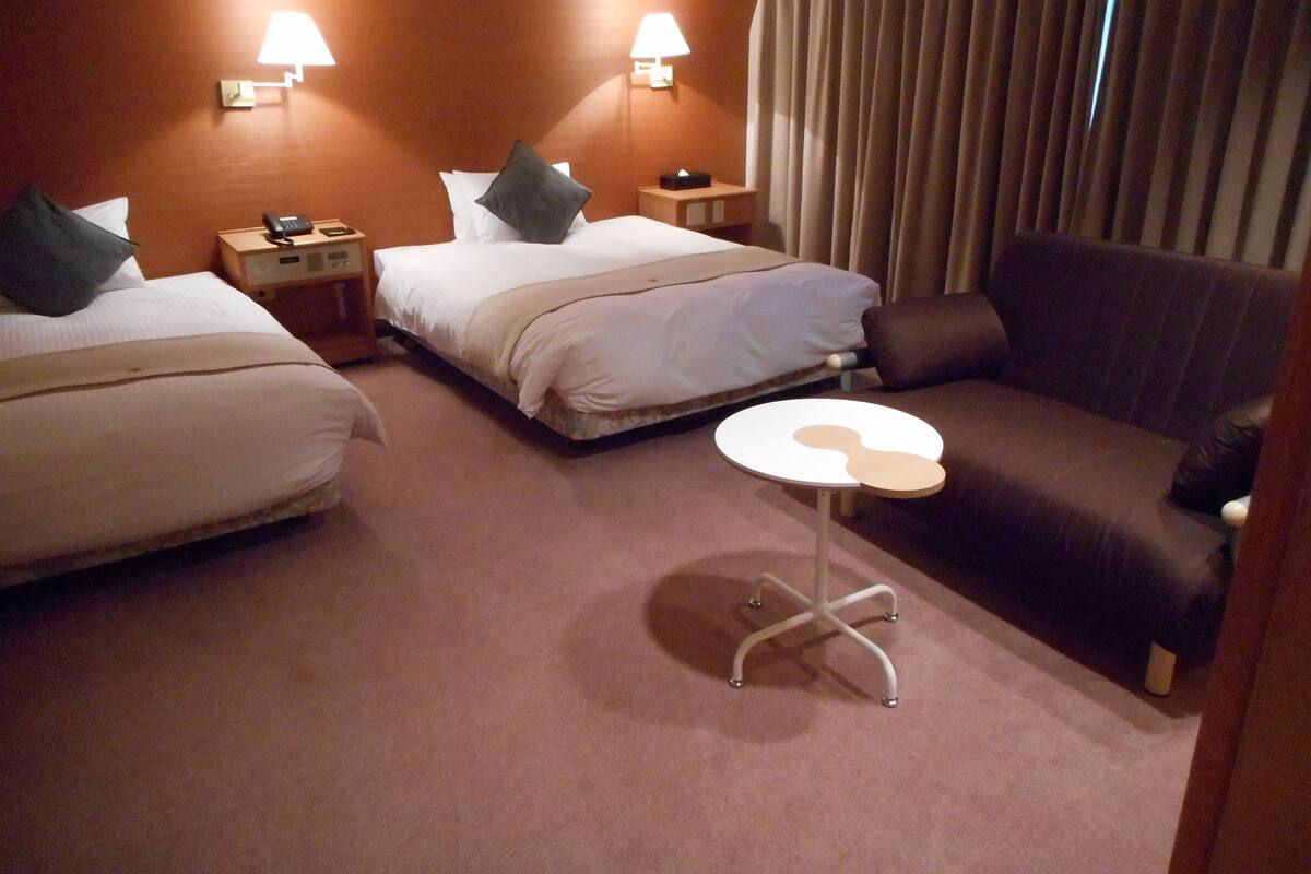 A hotel room with two beds, a sofa, a small round table, and two bedside lamps.