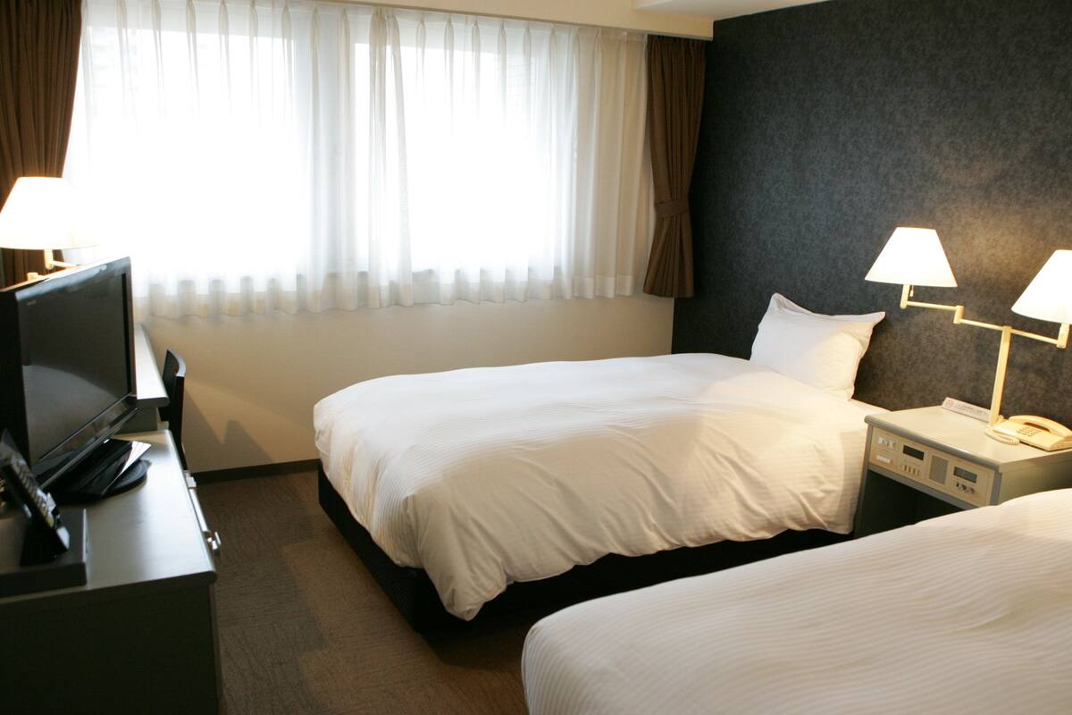 A hotel room with two beds, a TV, and bedside lamps.