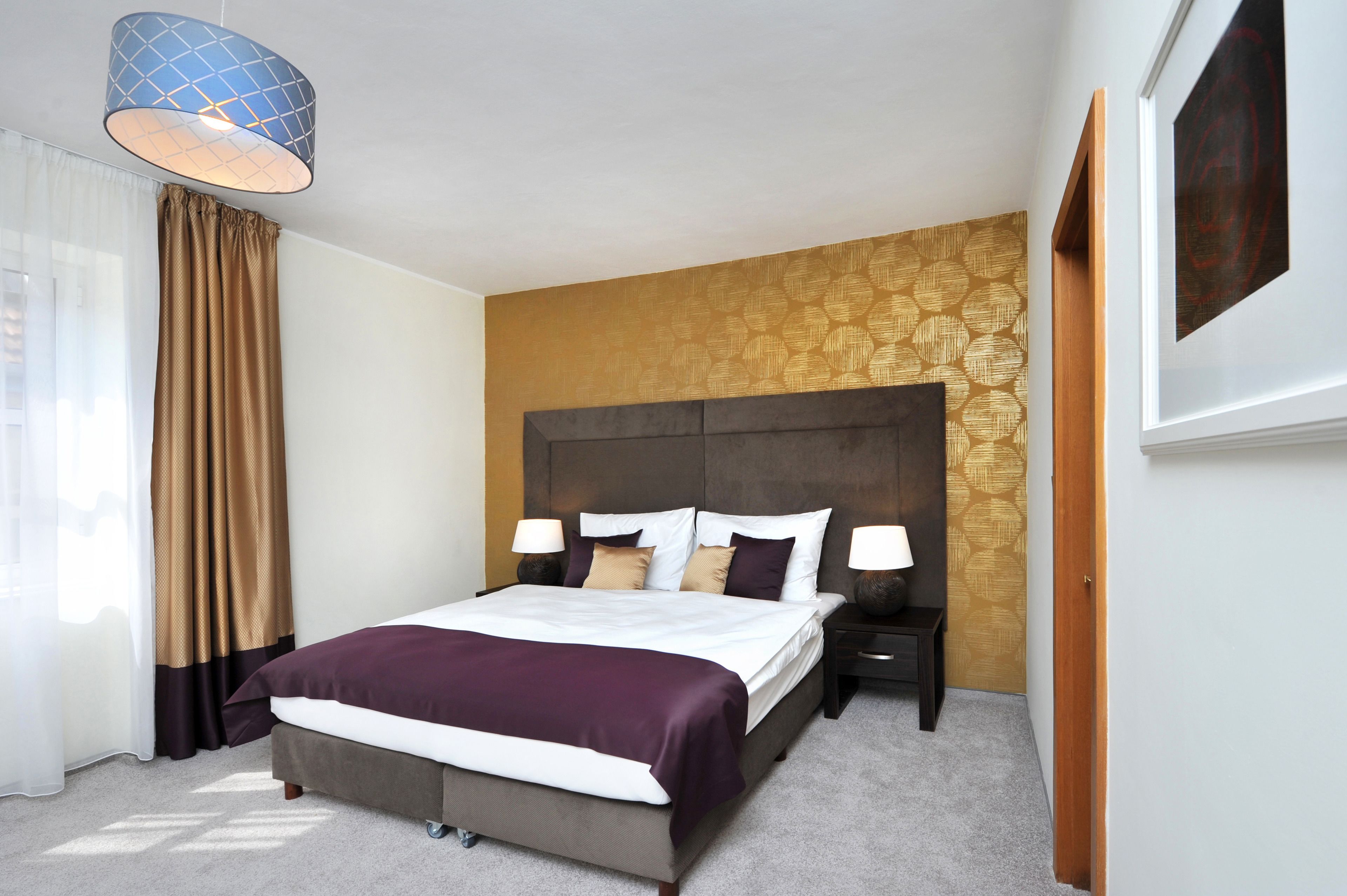 A hotel room with a large bed, two bedside tables with lamps, a headboard, and a window with curtains.