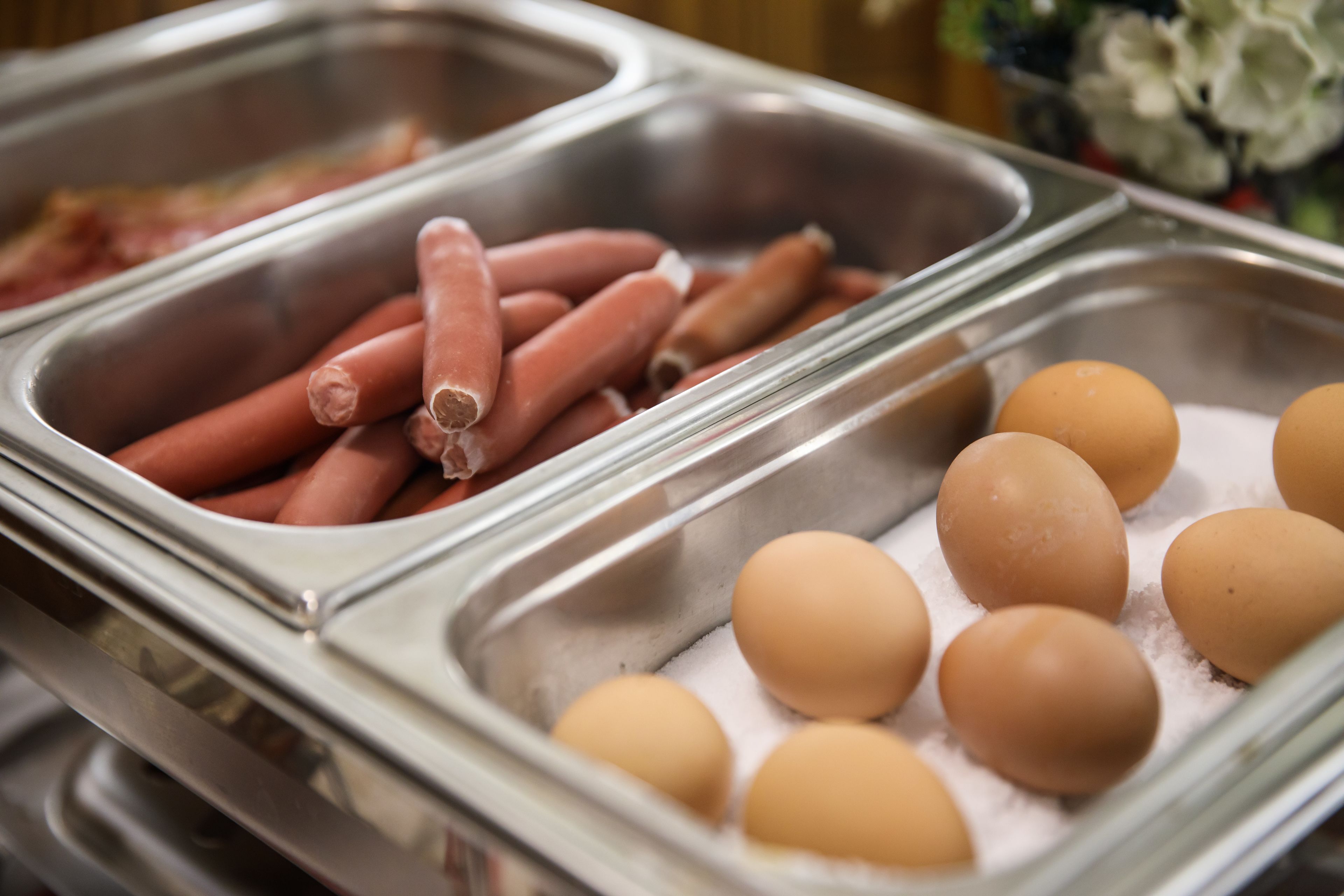 Un bufé con bandejas de hot dogs y huevos.