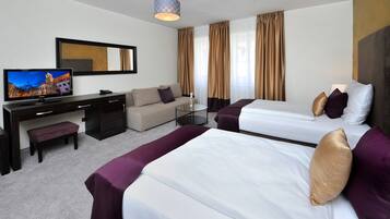 A hotel room with two beds, a sofa, a desk with a TV, and a large window with curtains.