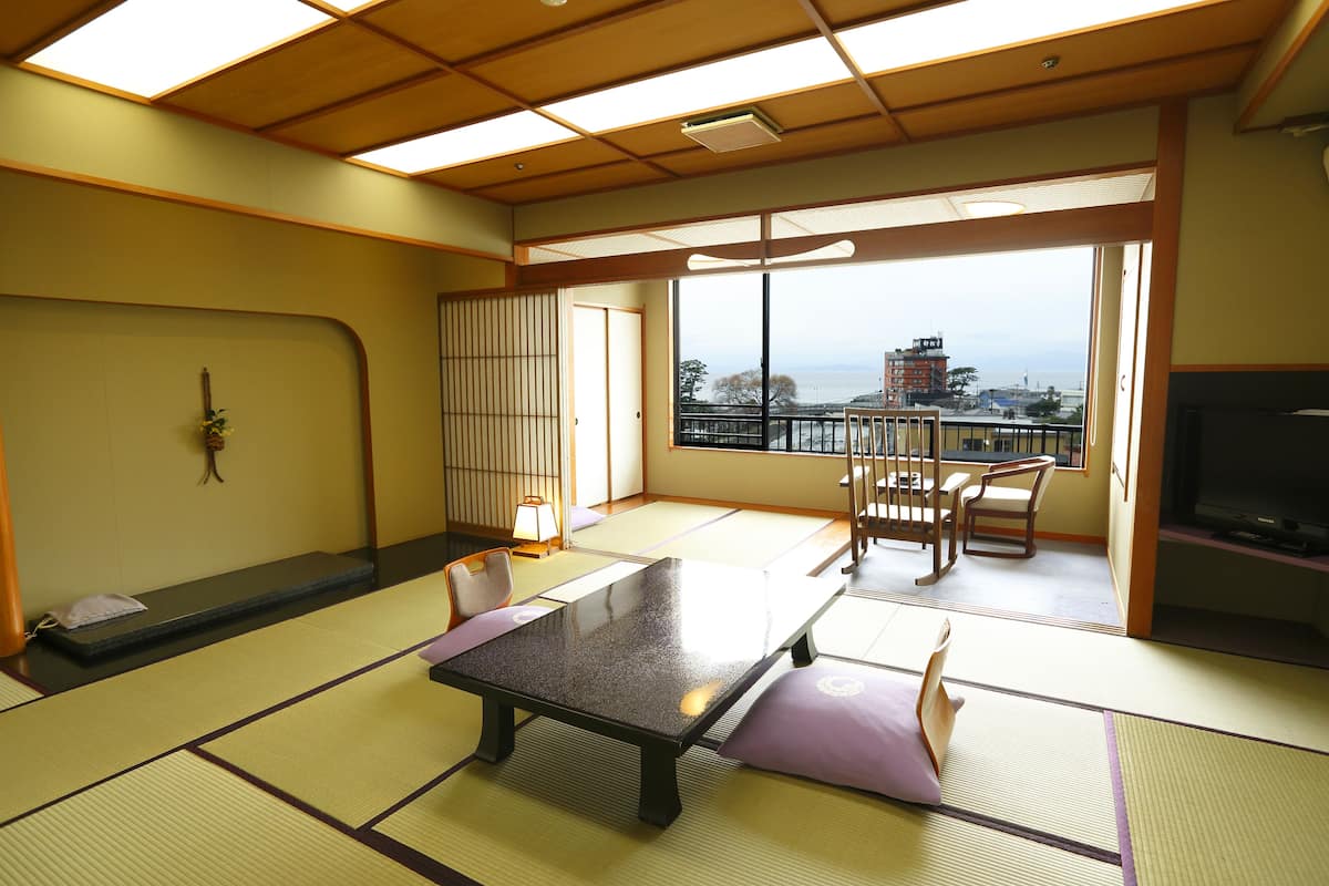A traditional Japanese room with tatami flooring, a low table, and a view of the city through large windows.