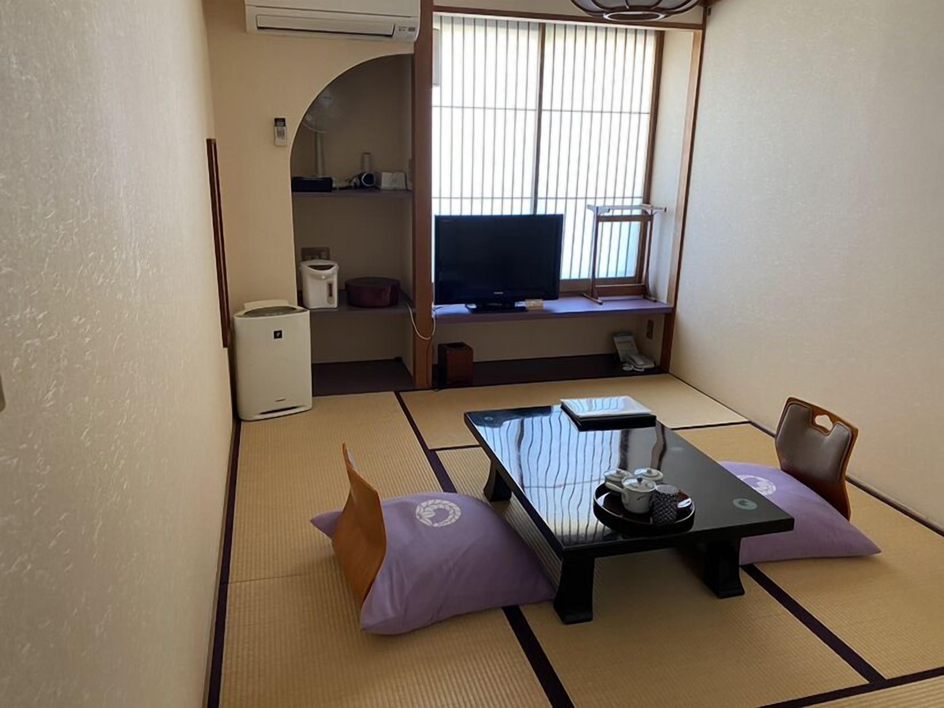 Habitació japonesa tradicional amb tatami, una taula baixa amb safata de vetjades i acompanyaments per al te, televisió a una estant i un petit armari.