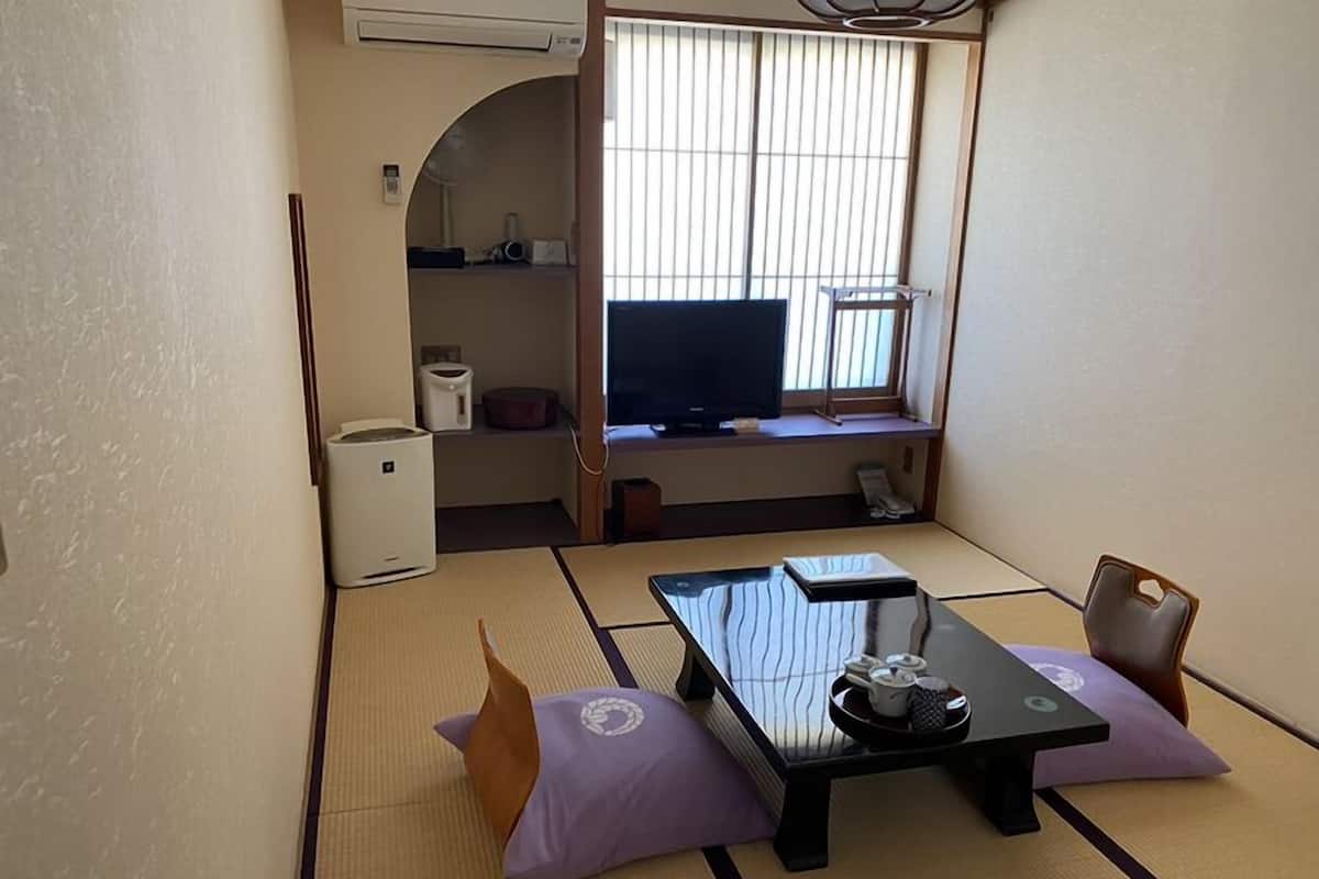 A traditional Japanese-style room with tatami flooring, a low table with a tray of tea utensils, a television on a shelf, and a small cabinet.