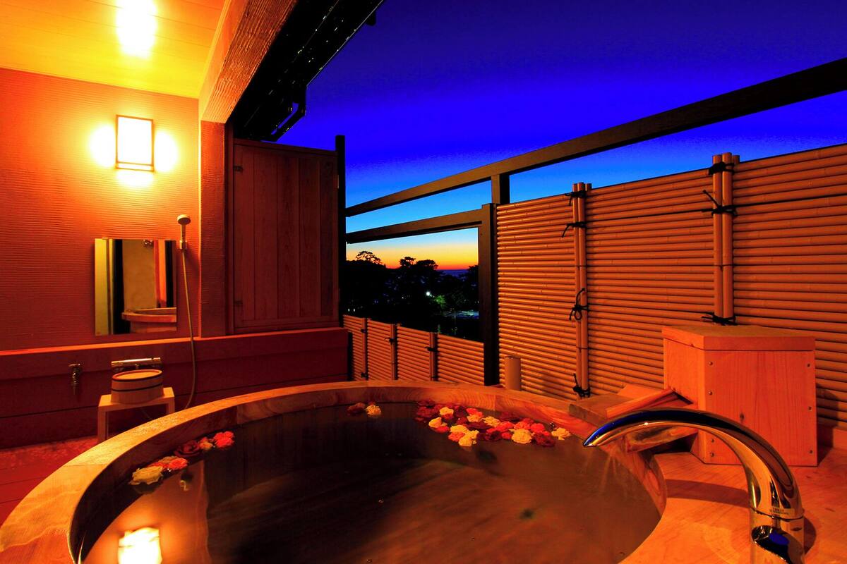 A modern bathroom with a large bathtub, a mirror, and a view of the sunset.