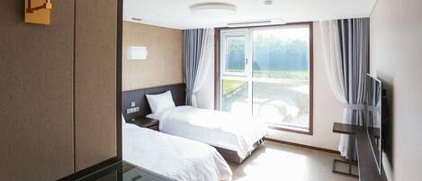 Habitación de hotel con dos camas, una mesita de vidrio, televisor y un amplio ventanal con cortinas.