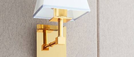 A wall-mounted lamp with a white shade and a gold base.