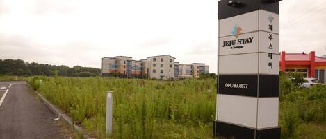 A Jeju Stay sign with a contact number, located in front of a row of modern apartment buildings.