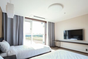 Habitación de hotel con dos camas, televisor de pantalla plana, ventilador de techo y un ventanal grande con cortinas.
