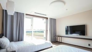 A modern hotel room with a large bed, a flat-screen TV mounted on the wall, and a sliding glass door leading to a balcony. - Jeju Stay in Seongsan Hotel (Seogwipo)