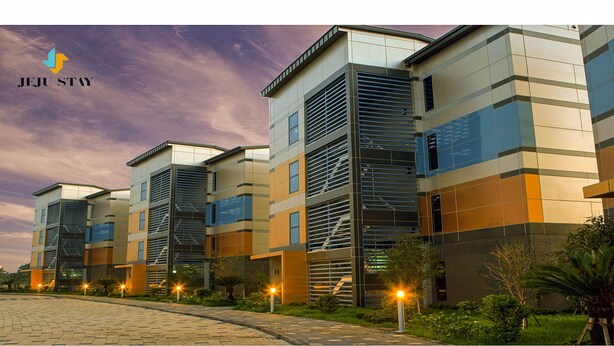 A modern hotel with a multi-story structure, featuring a mix of glass and metal facades, and a landscaped outdoor area with pathways and greenery. - Jeju Stay in Seongsan Hotel (Seogwipo)