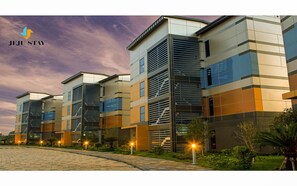 A modern hotel with a multi-story structure, featuring a mix of glass and metal facades, and a landscaped outdoor area with pathways and greenery. - Jeju Stay in Seongsan Hotel (Seogwipo)