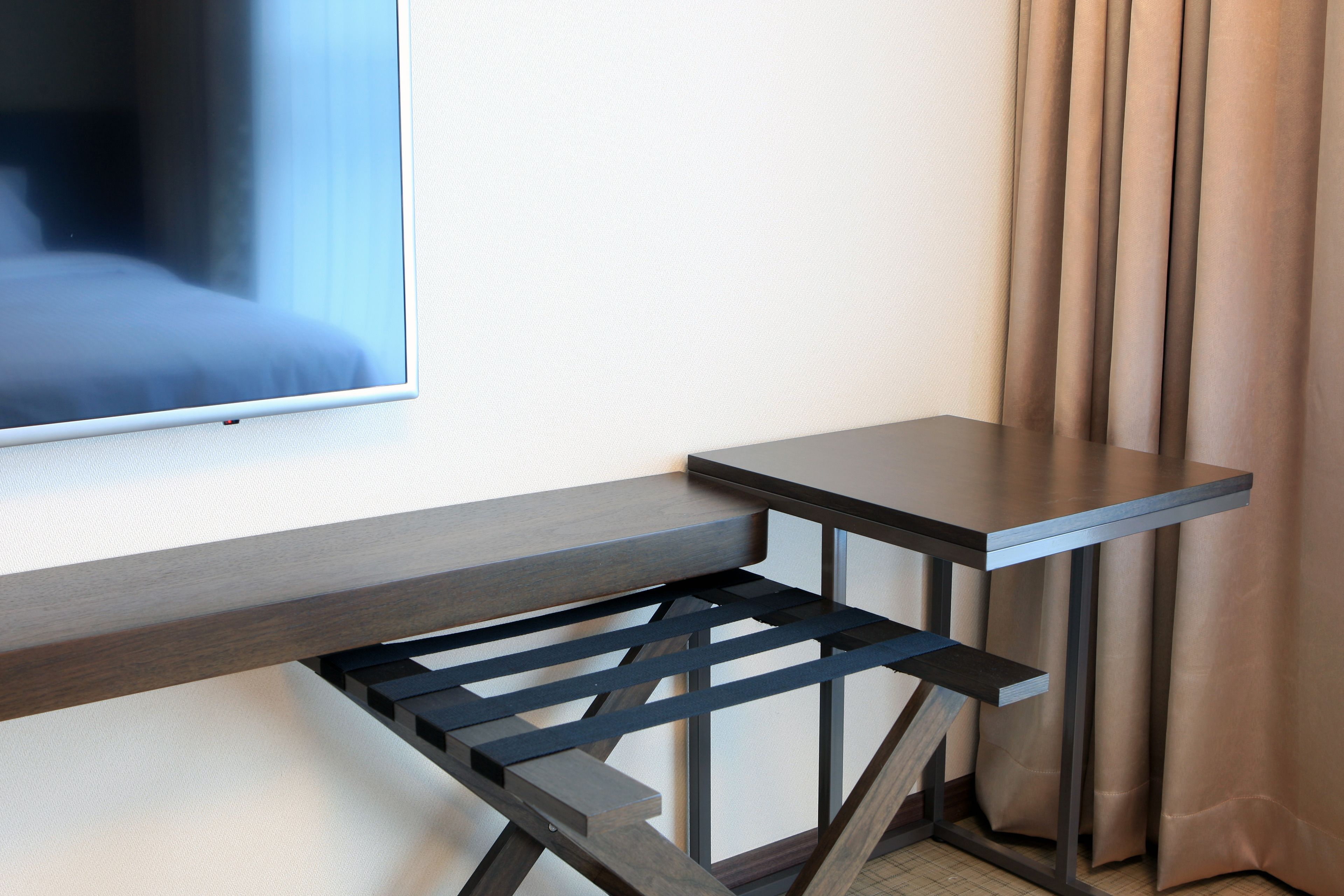 A modern room with a bed, a TV mounted on the wall, a small table, and a window with curtains.