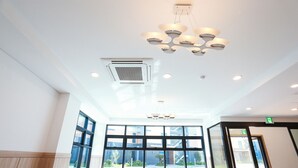 A spacious lobby with large windows, a modern chandelier, and an emergency exit sign. - Jeju Stay in Seongsan Hotel (Seogwipo)