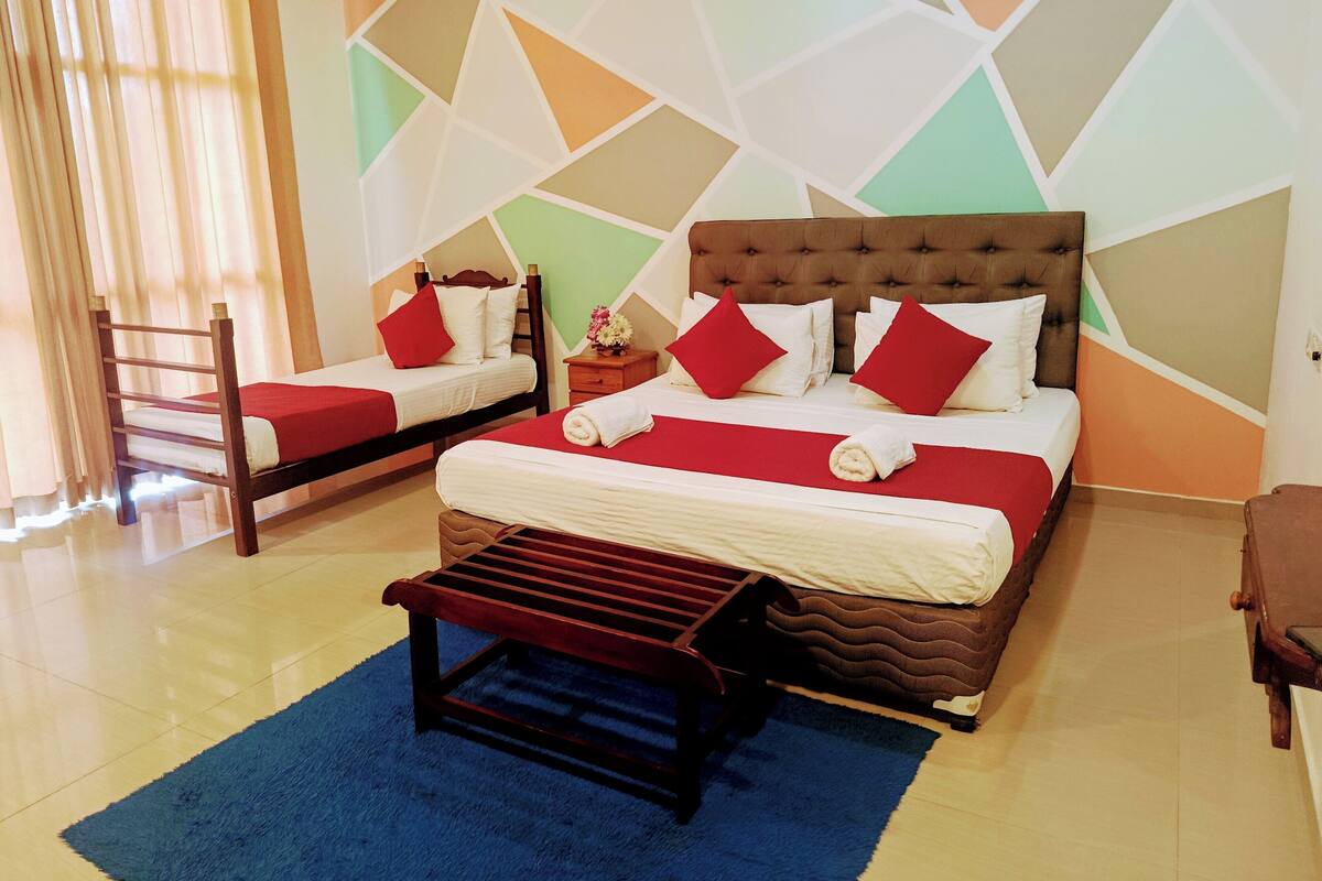 A hotel room with two beds, a wooden bench, a blue rug, and a geometric-patterned wall.
