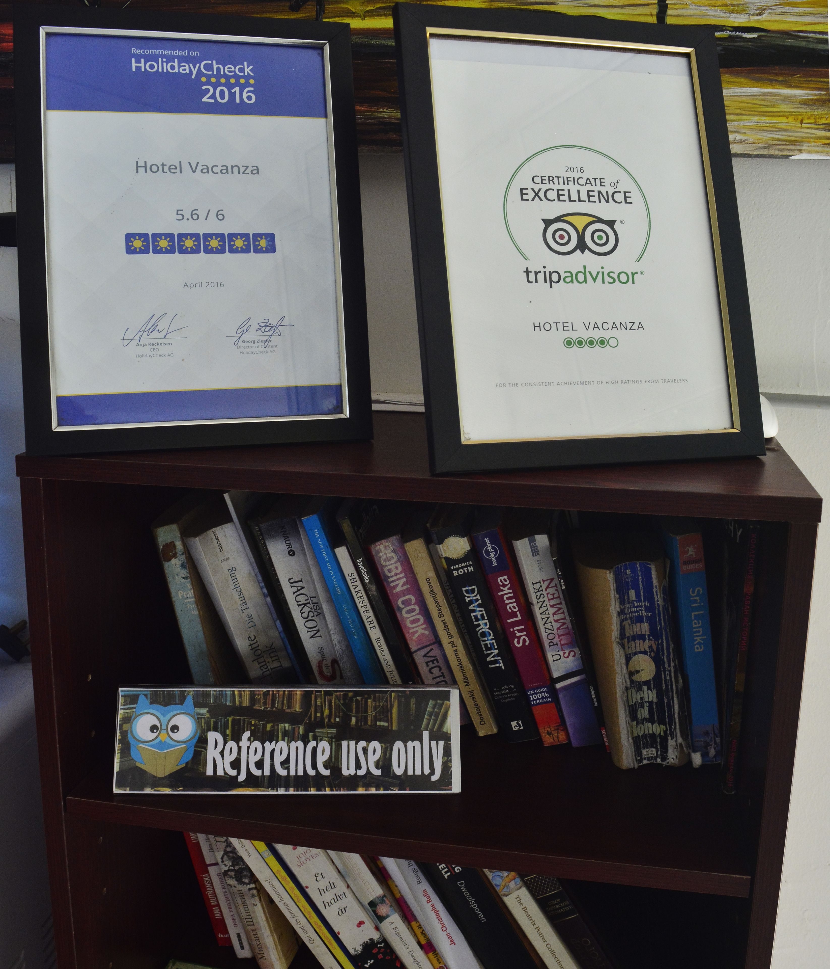 Two framed certificates on a shelf, one from HolidayCheck 2016 and another from TripAdvisor, both related to Hotel Vacanza.