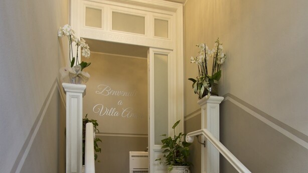 A marble staircase with white railings and a chandelier, leading to a door with a sign reading "Welcome to Villa Aria." - Villa Anna (Lucca)
