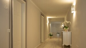 A hallway with a wooden floor, a white door, and a small table with a vase of flowers. - Villa Anna (Lucca)