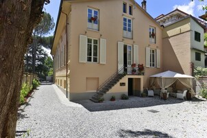 Un edificio a due piani con un cortile in ghiaia, una scala che conduce al piano superiore e un'area salotto esterna con tavolo e sedie.