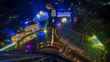 Vista nocturna de un edificio con senderos e instalaciones iluminadas, incluyendo una escalera en espiral y una zona de piscina.