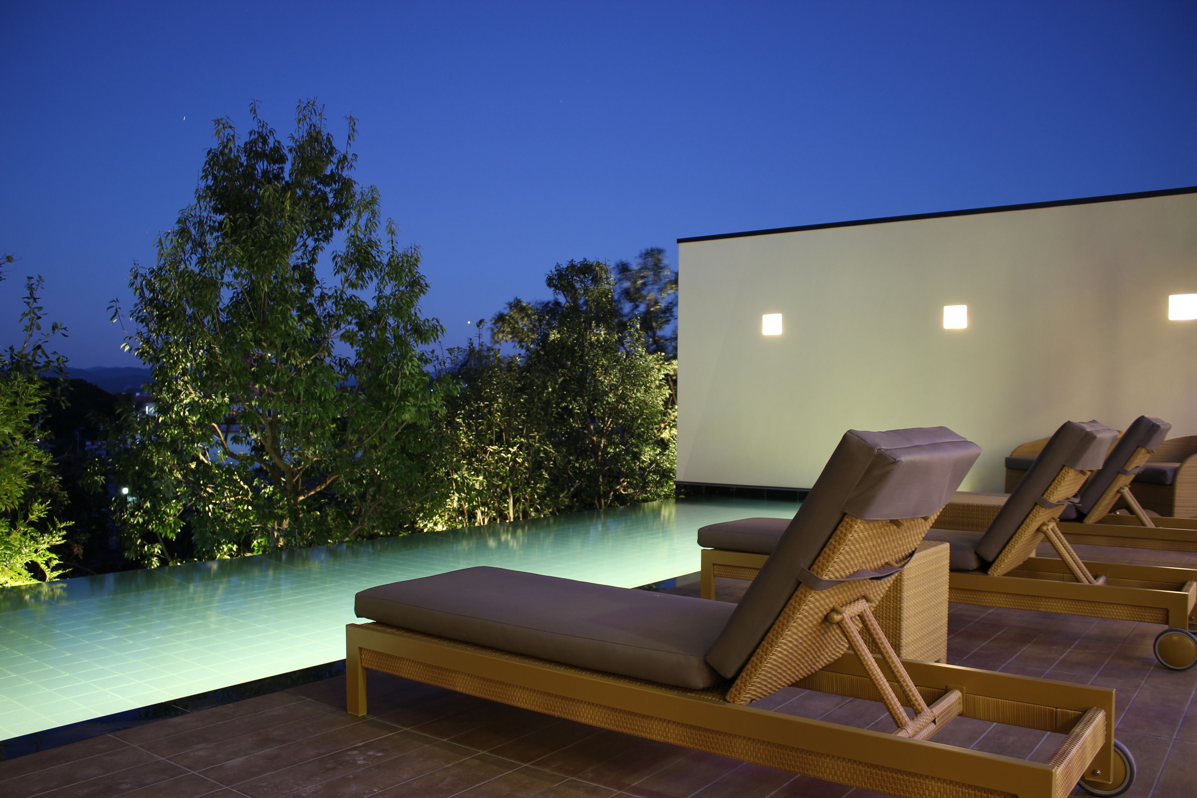 A rooftop infinity pool with lounge chairs and a large screen.