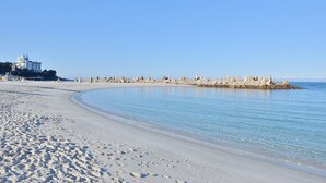A sandy beach with clear blue water, a rocky breakwater, and a building in the background. - Shirahama Coganoi Resort&Spa (Shirahama)