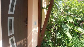 Una puerta de madera con tres abertura rectangulares, una rejilla de metal y un jardín con varias plantas y un árbol.