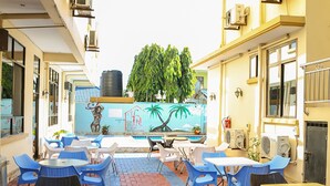 Un patio al aire libre con mesas y sillas, un mural en la pared y una piscina al fondo.