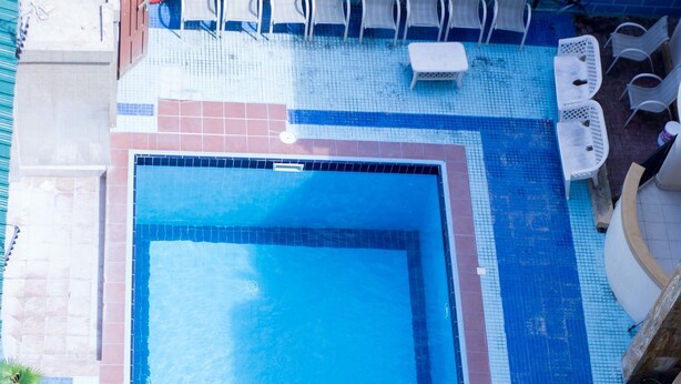 Una piscina con una persona nadando, rodeada de sillas de descanso y una zona de terraza con baldosas.
