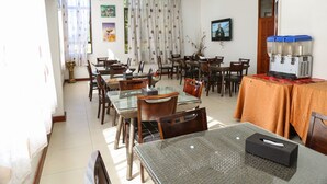 Un comedor amplio con varias mesas y sillas, un televisor montado en la pared y un dispensador de agua a la derecha.