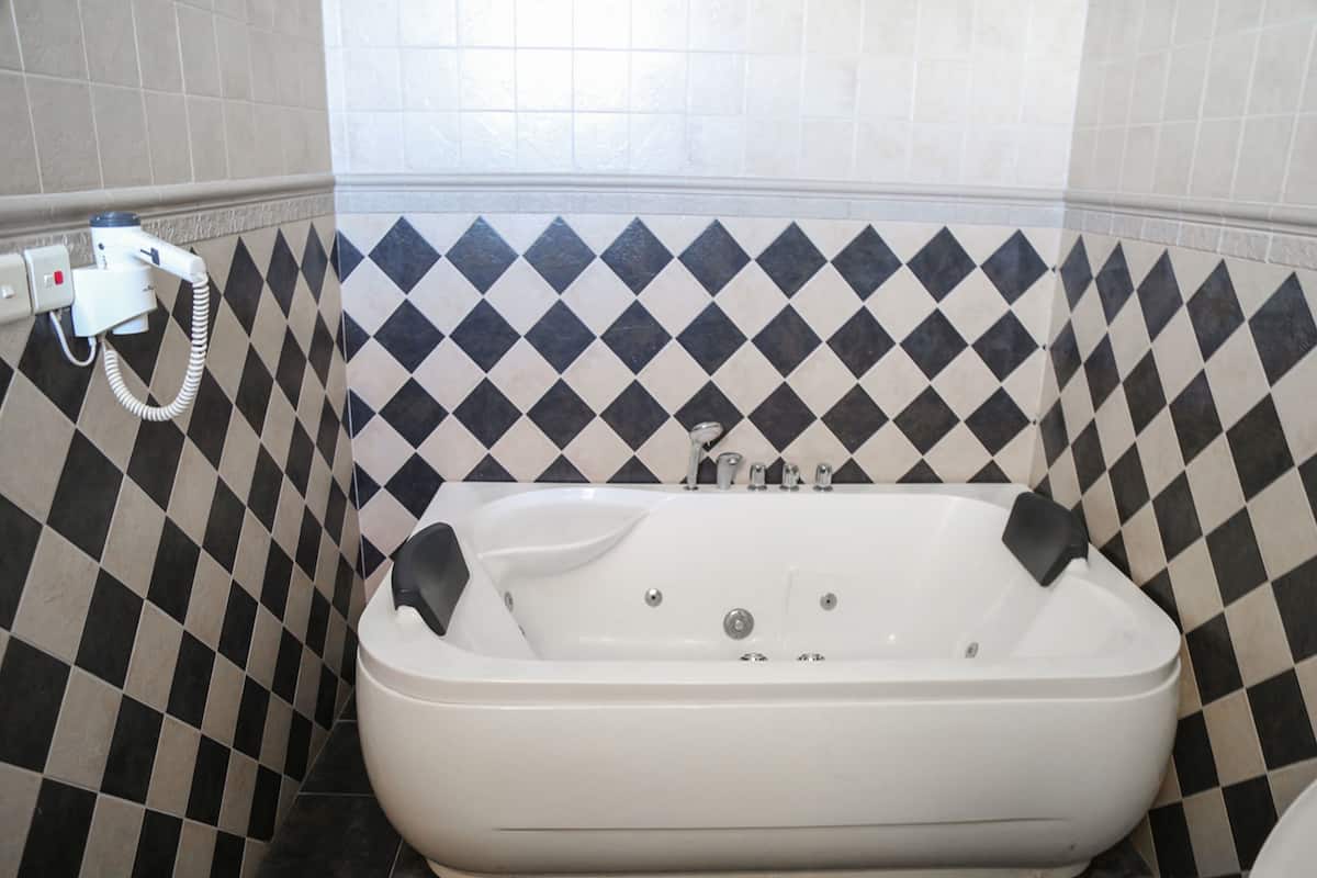 Une salle de bain avec un mur recouvert de carreaux noirs et blancs formant un motif à damier, une baignoire blanche et des toilettes blanches.