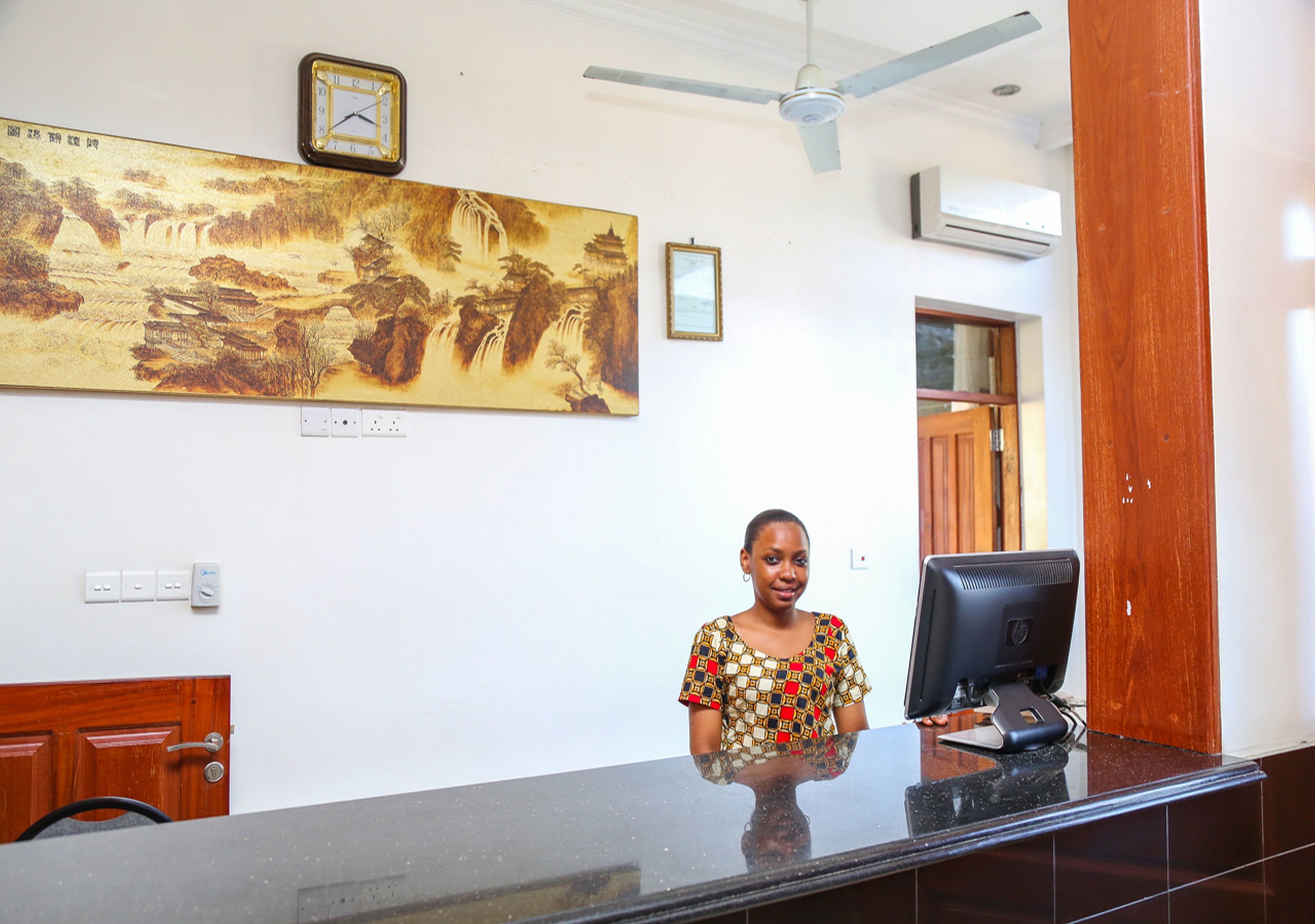 A reception desk with a computer monitor, a painting of a landscape, and a ceiling fan.